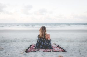 Caucasian woman shitting on a beach facing the ocean