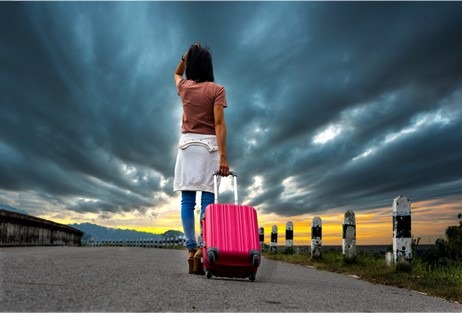 Woman with pink suitcase looking up at a stormy sky